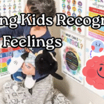 Child holding a stuffed animal while pointing to colorful emotion with bold text overlay that reads ‘Helping Kids Recognize Their Feelings.’